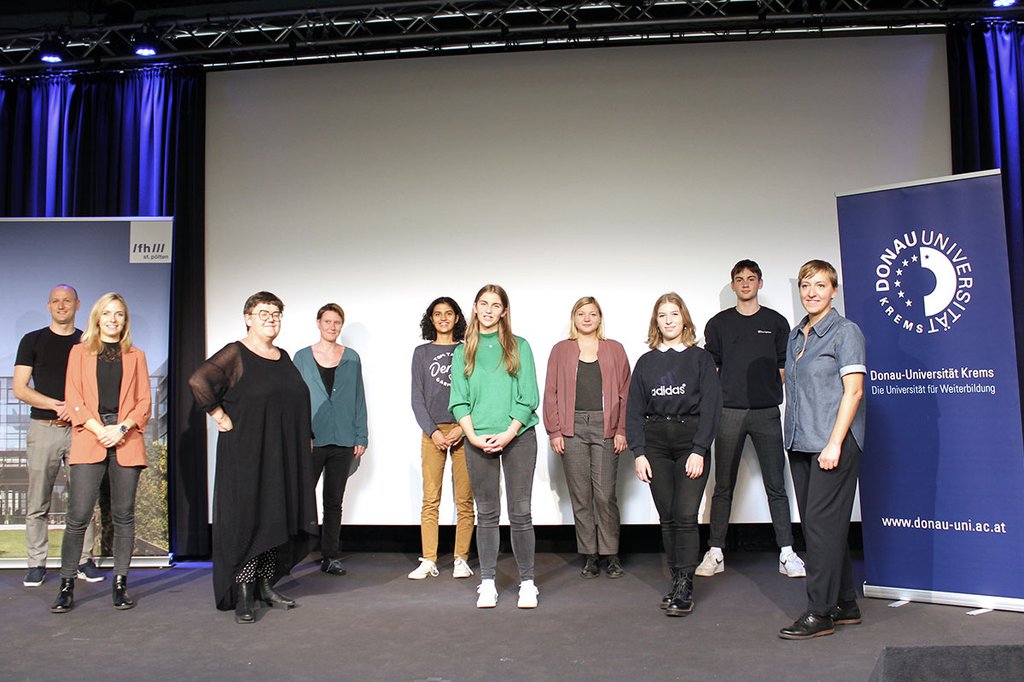 Verschiedene Akteur*innen der Studie "Wie Jugendliche in digitalen Räumen politisieren" bei der Abschlusskonferenz auf der Bühne, an der Seite sind jeweils Roll-ups der beiden Hochschulen – Donau-Universität Krems und FH St. Pölten